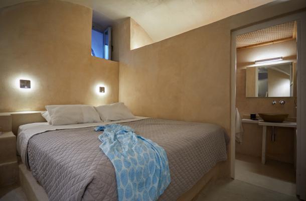 A cozy bed with a blue blanket and white pillow in a charming cellar accommodation in oia santorini hu17649566545412288139.jpg