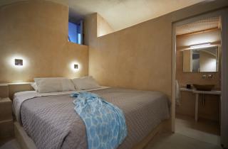 A cozy bed with a blue blanket and white pillow in a charming cellar accommodation in oia santorini hu 30847b1850699e66.jpg