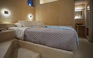 A cozy bed with a blue blanket in a charming cellar accommodation in oia santorini hu 1e68c4e154f819ba.jpg