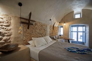 A cozy bedroom with stone walls featuring a bed private hot tub and a veranda in oia santorini hu8649105497665696334.jpg