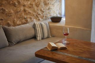 A cozy couch with a book and a glass of wine set in a luxurious oia accommodation with a private hot tub hu16255055715114862721.jpg