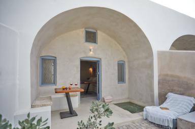 A cozy patio with a table and chair leading to a door set in oia santorini featuring a private hot tub and courtyard.jpg